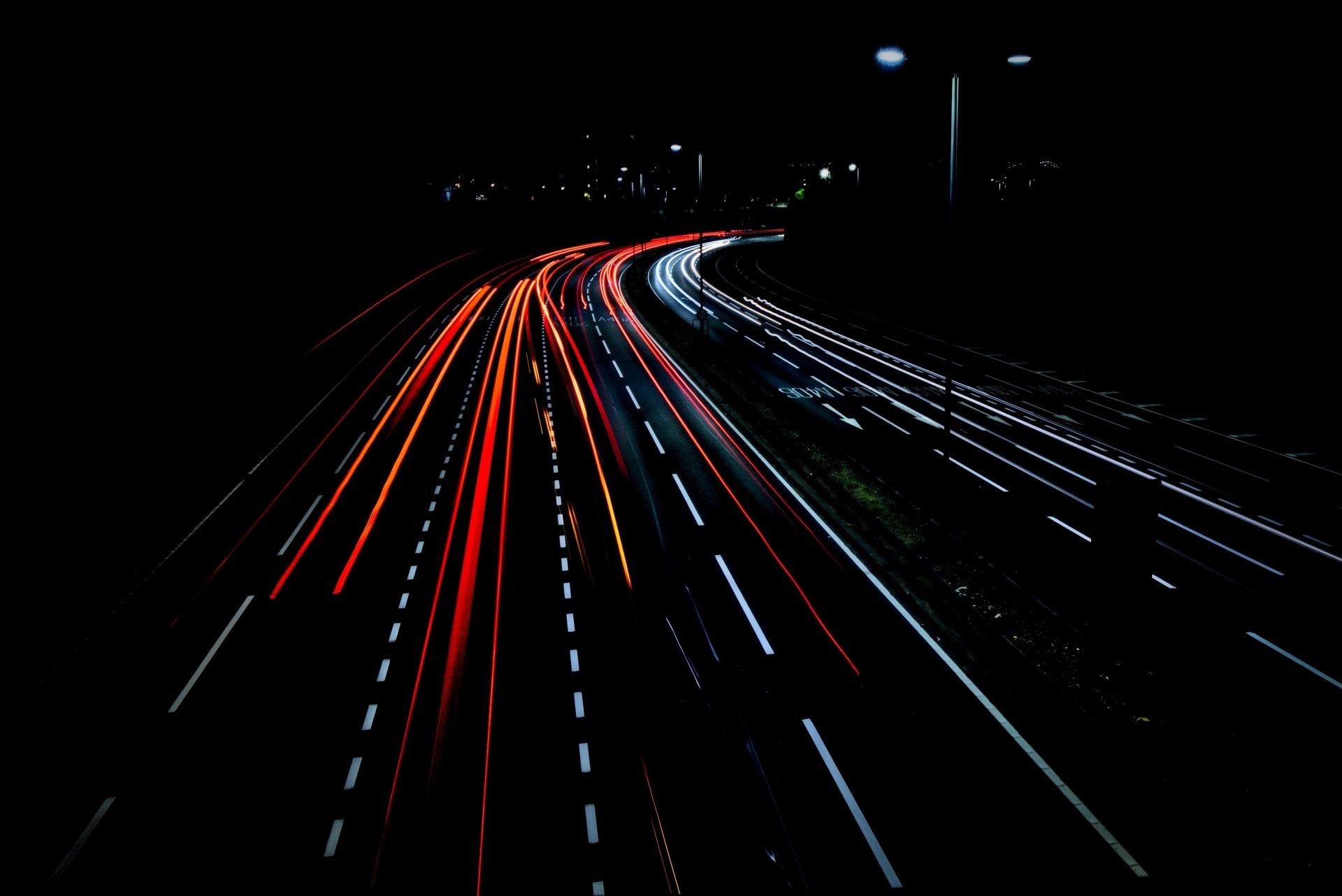 A 4K Ultra HD time-lapse photo of a night road showing streaks of red and white lights from moving vehicles against a dark background.