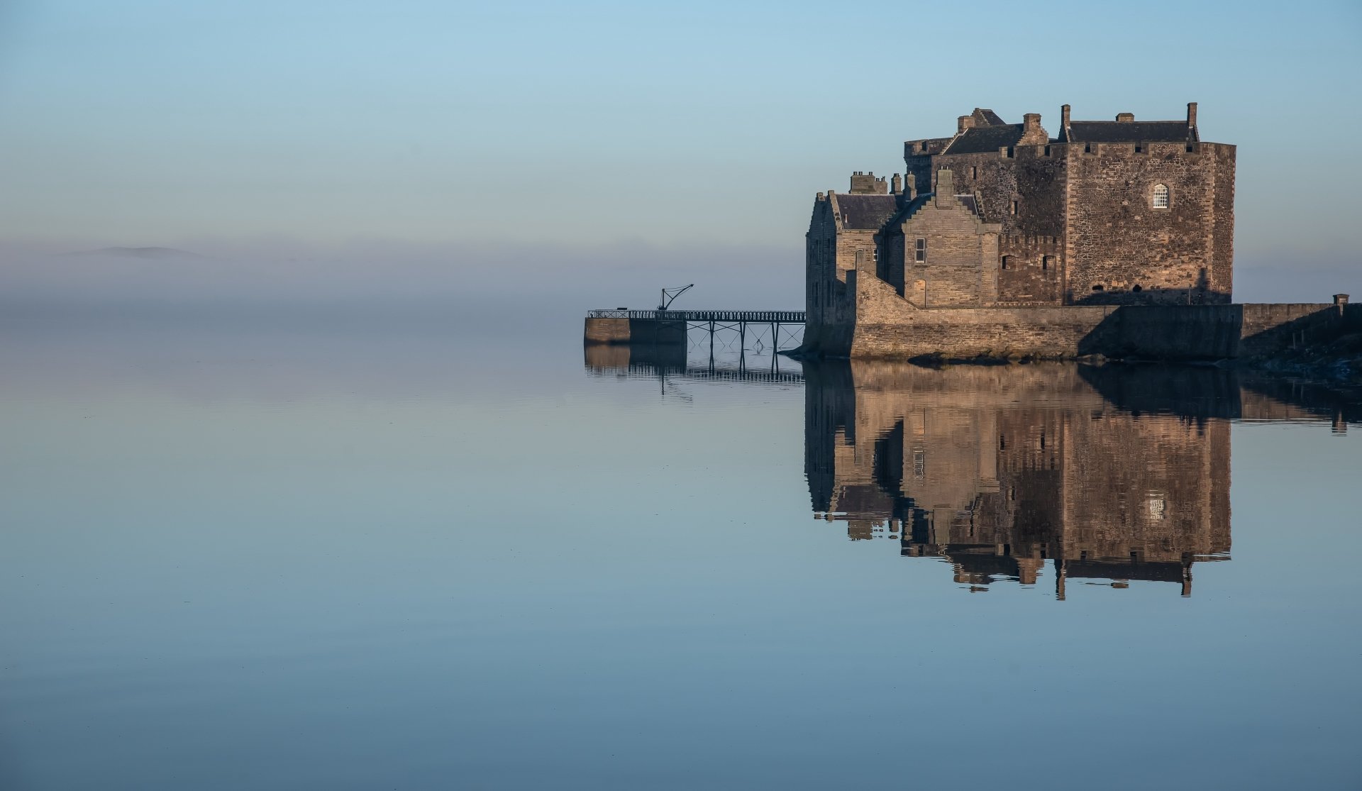 4K Ultra HD image of a foggy Scottish castle with a clear reflection on still water, showcasing a historic man-made structure in a serene landscape.