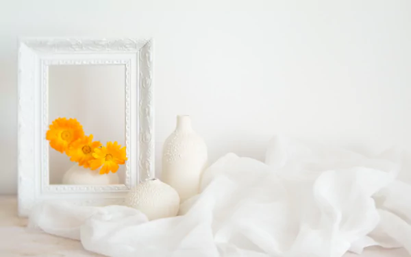 Minimal still-life photography: bright calendula in a white vase and jug beside an ornate white frame and draped fabric — 2K Quad HD PC desktop wallpaper/background.