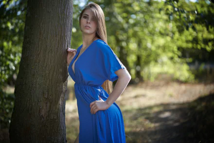 Brunette model with long hair in a flowing blue dress poses by a tree; shallow depth of field. 4K Ultra HD PC desktop wallpaper background.