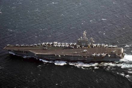A high-definition aerial view of the USS Dwight D. Eisenhower (CVN-69) aircraft carrier underway, showcasing its military navy warship and deck full of aircraft.