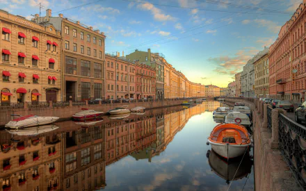 Scenic view of a man-made river in Saint Petersburg, Russia, with historic buildings lining the waterfront and boats docked along the calm water under a vibrant sky.