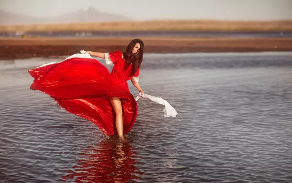 HD PC desktop wallpaper and background: woman in a flowing red dress wading through shallow water, moody windswept shoreline with billowing fabric.