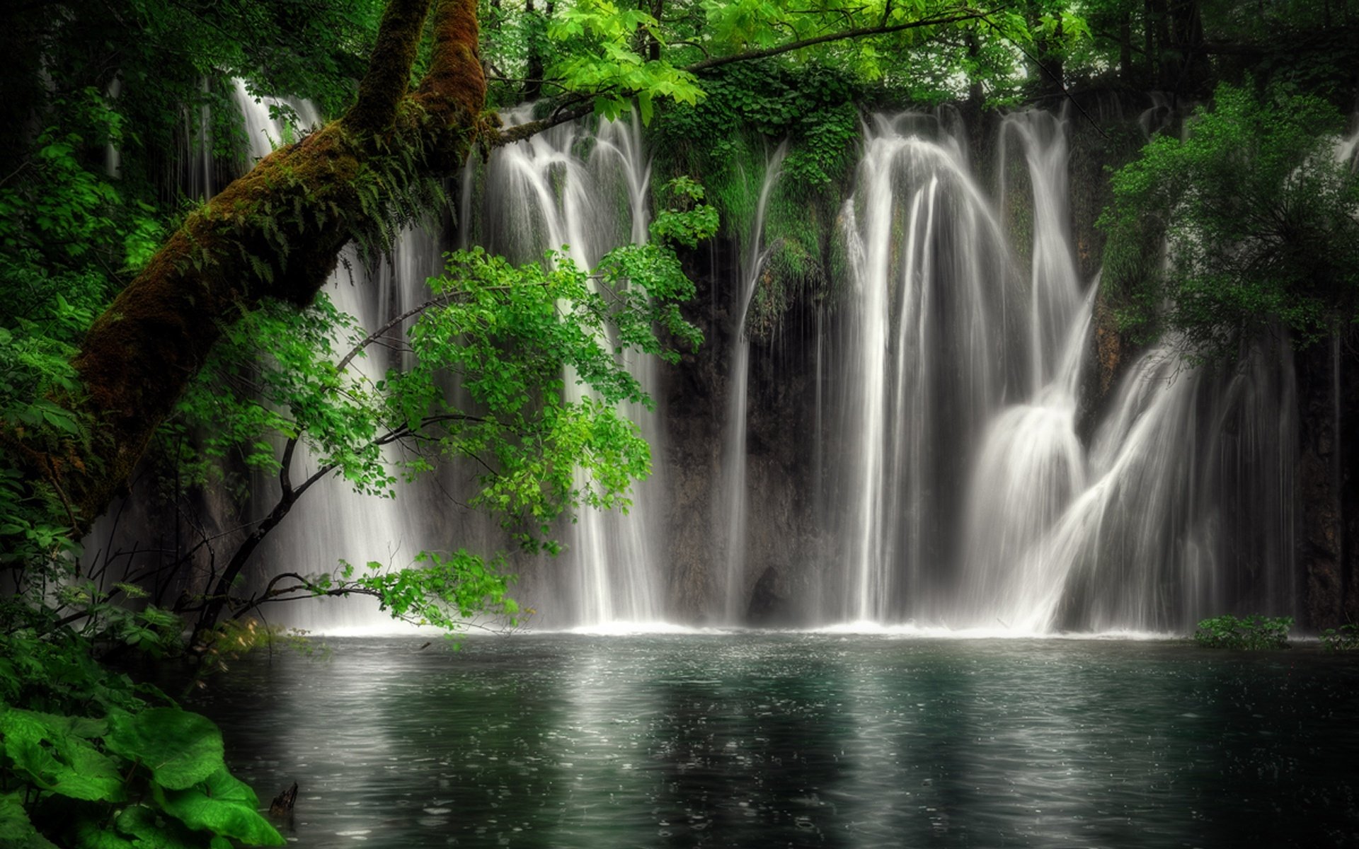 HD PC desktop wallpaper featuring a serene waterfall cascading through lush green vegetation in a vibrant natural setting.