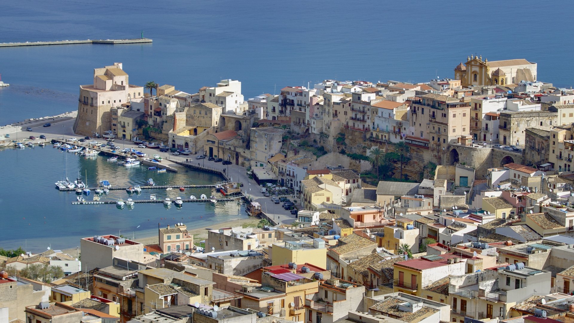 4K Ultra HD desktop wallpaper of Castellammare del Golfo, Sicily, Italy: sunlit coastal town with man-made harborfront buildings and rows of houses lining the water.
