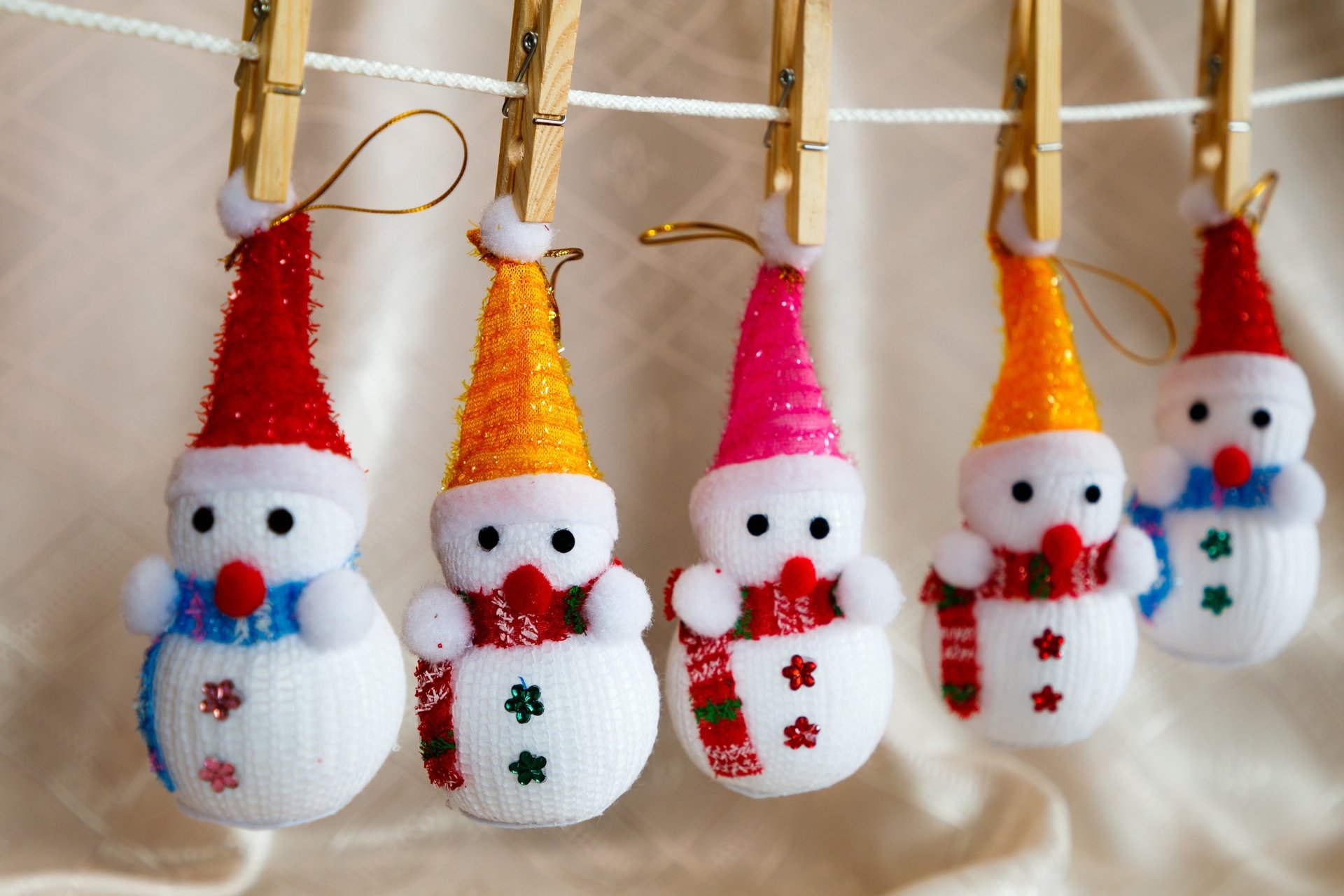 Knitted snowman ornaments clipped to a line with clothes pins, bright hats and scarves in festive Christmas photography — 2K Quad HD PC desktop wallpaper/background.