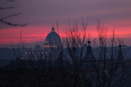 HD desktop wallpaper: St. Peter's Basilica silhouetted against a pink-purple evening sky over the Vatican in Rome, with bare branches in the foreground.
