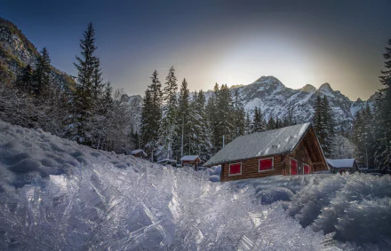 HD PC desktop wallpaper photograph: snow-covered cabin and fir trees beneath snowy mountain peaks, red house in serene winter nature.
