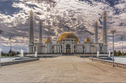HD PC desktop wallpaper/background featuring a grand religious mosque in Ashgabat, Turkmenistan — golden dome and soaring minarets beneath dramatic cloud-filled sky.