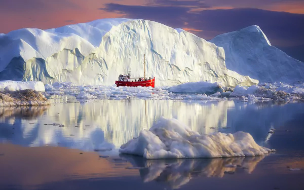 A red ship navigates icy Arctic waters near a massive iceberg in Greenland, its reflection mirrored on the calm surface in this HD desktop wallpaper.