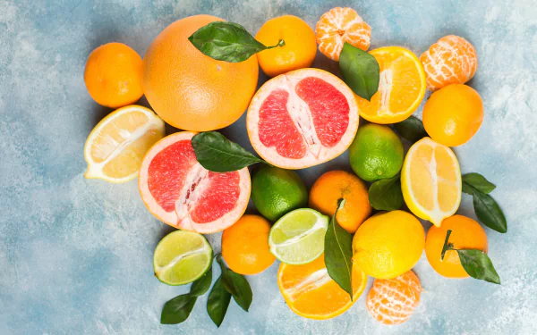 2K Quad HD desktop wallpaper of citrus assortment—grapefruit halves, lemons, limes, oranges and mandarins with leaves on a cool blue textured background.