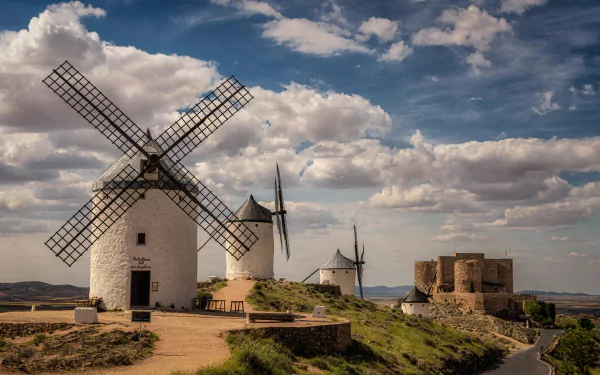 2K Quad HD PC desktop wallpaper: Spanish hilltop scene of white man-made windmills and a medieval stone castle beneath dramatic clouds.