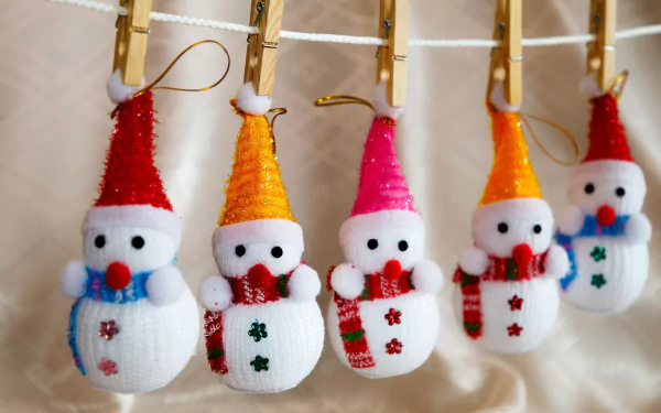 Knitted snowman ornaments clipped to a line with clothes pins, bright hats and scarves in festive Christmas photography — 2K Quad HD PC desktop wallpaper/background.