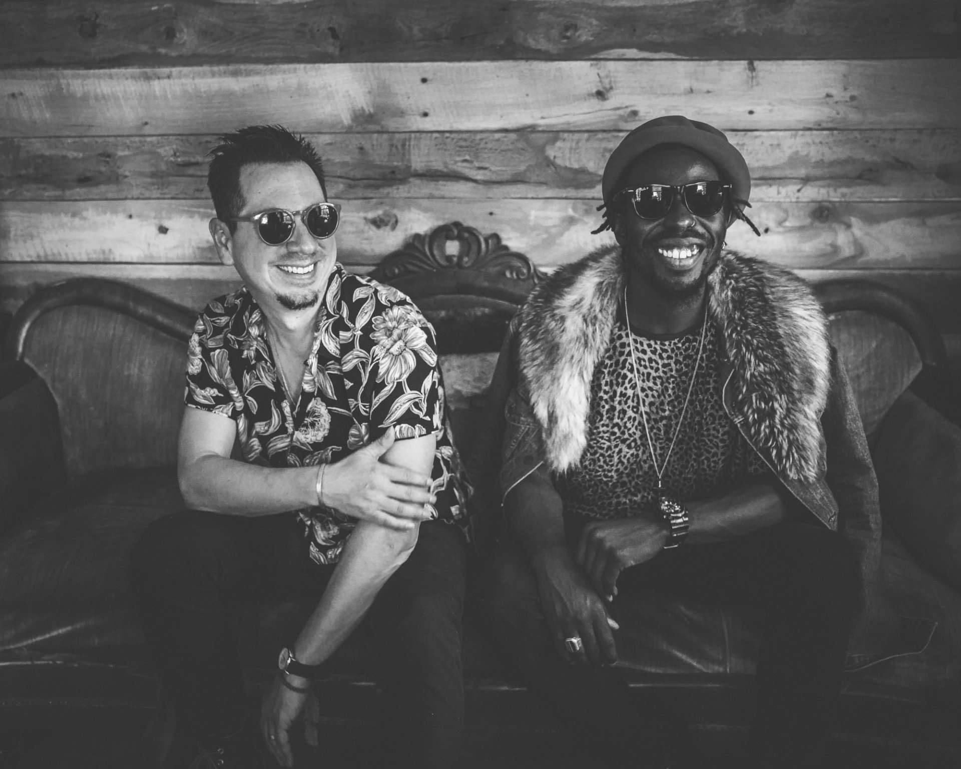 Black Pumas band members smile and pose casually on a vintage sofa, creating a vibrant atmosphere in this HD desktop wallpaper background.