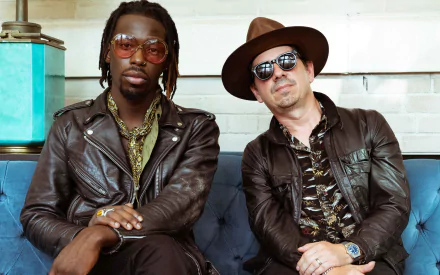 HD wallpaper featuring two stylish men seated on a blue couch, exuding cool confidence, representing the essence of Black Pumas.