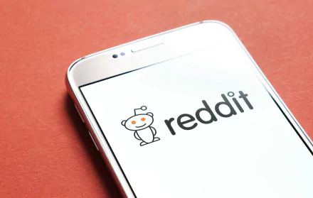 HD desktop wallpaper featuring a mobile phone with the Reddit logo displayed on its screen, set against a red background.