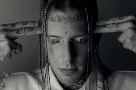 HD desktop wallpaper of a person with facial tattoos and pierced nose, holding fingers to head in a black and white photo.