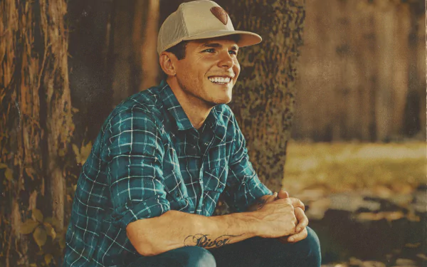 HD desktop wallpaper featuring Granger Smith in a blue plaid shirt and hat, smiling while seated outdoors against a tree.