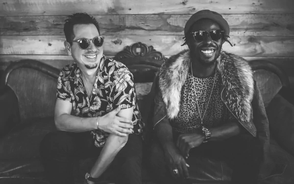 Black Pumas band members smile and pose casually on a vintage sofa, creating a vibrant atmosphere in this HD desktop wallpaper background.