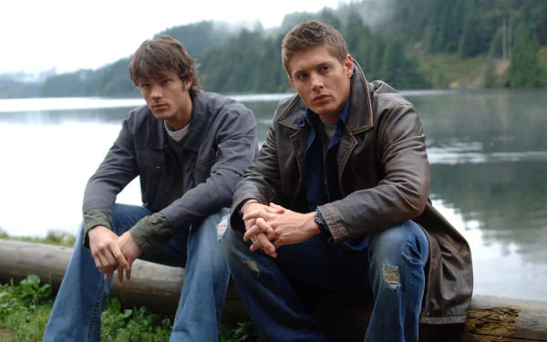 Sam Winchester and Dean Winchester from the TV show Supernatural, portrayed by Jared Padalecki and Jensen Ackles, sit by a lakeside in this 4K Ultra HD desktop wallpaper.