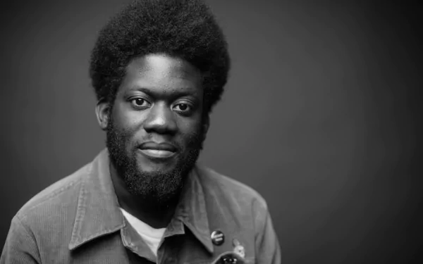 A black and white HD desktop wallpaper featuring musician Michael Kiwanuka, showcasing his distinctive afro and thoughtful expression against a simple background.