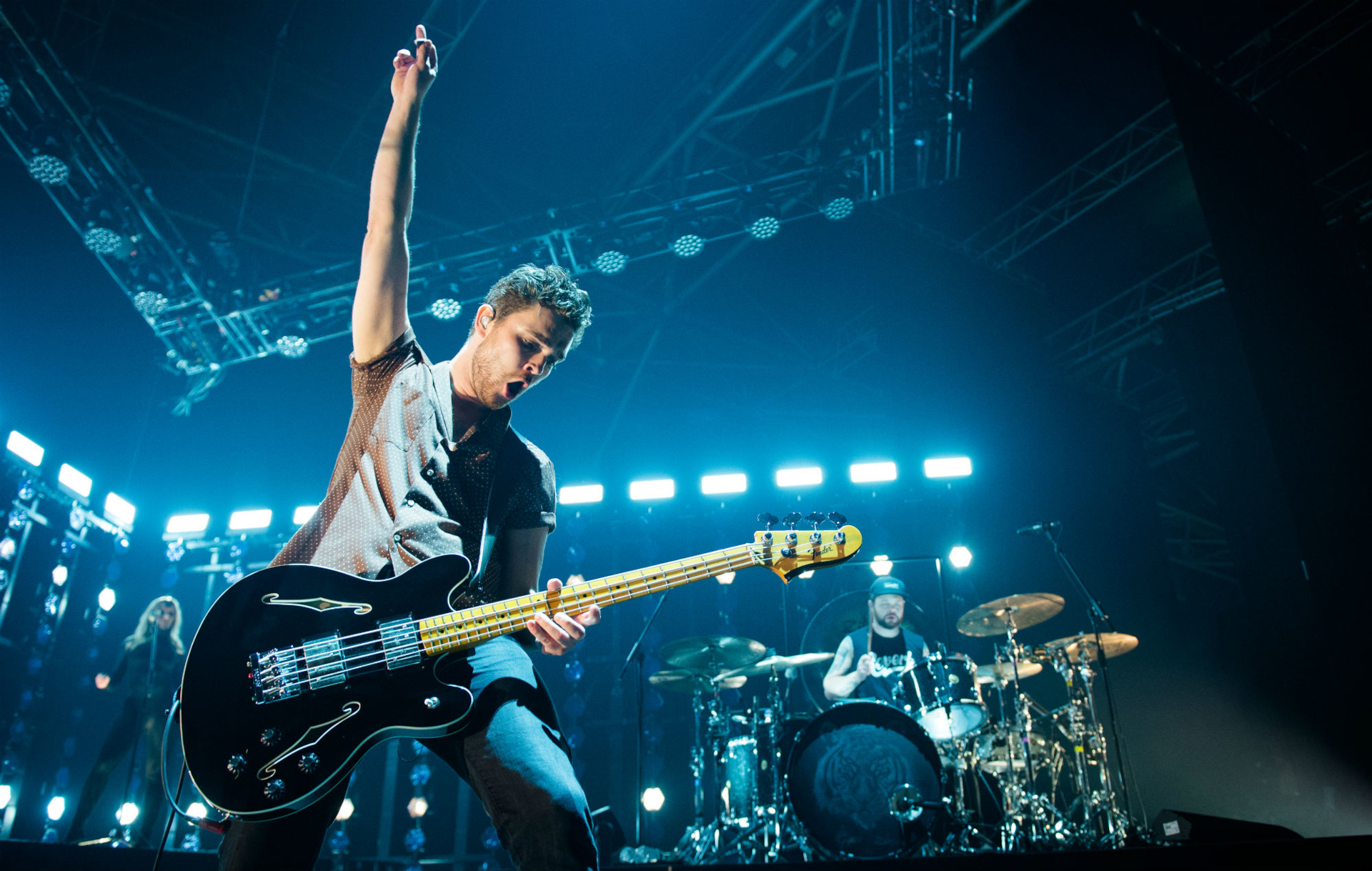 HD desktop wallpaper of Royal Blood musicians performing live on stage, featuring a dynamic shot of the bassist in the foreground and the drummer in the background, surrounded by vibrant stage lighting.