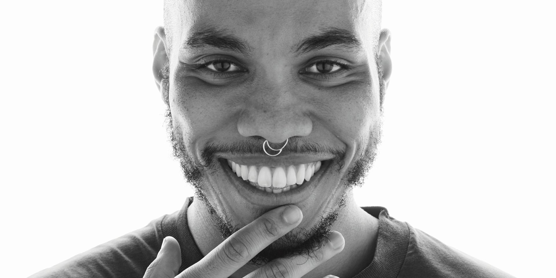 Black and white HD wallpaper of a smiling man with a nose ring, offering a bright and cheerful background.