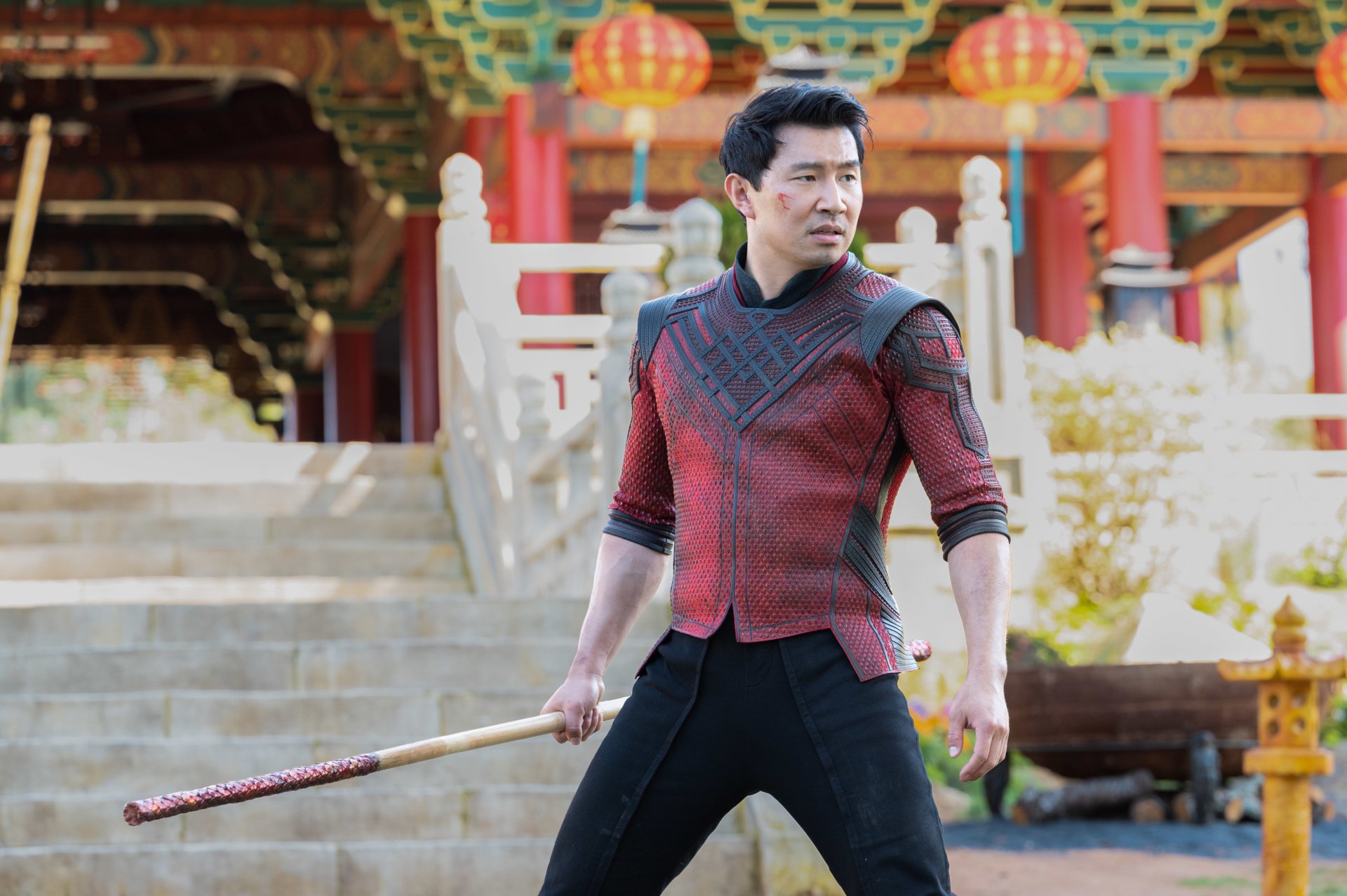 Simu Liu as Shang-Chi in a detailed 4K Ultra HD movie wallpaper, set against a traditional Asian architectural background, wielding a staff in a dynamic pose.