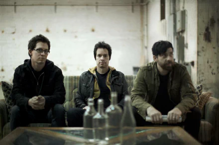 HD desktop wallpaper featuring three members of the band Chevelle, seated informally in a room with a rustic ambiance.