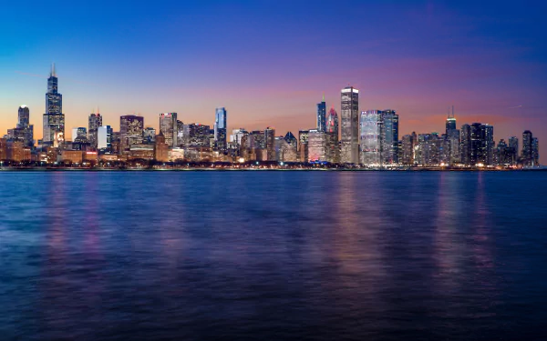 5K Ultra HD PC desktop wallpaper of Chicago, Illinois skyline at night — man-made skyscrapers and city buildings glowing and reflecting on Lake Michigan.