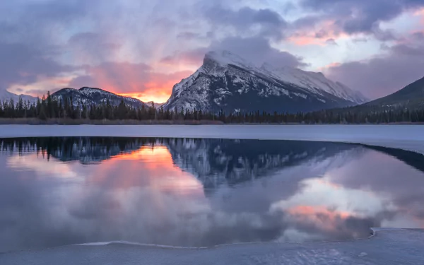 Winter dawn over a snow-capped mountain in Banff National Park, Canada, reflected in the calm lake waters, captured in stunning 4K Ultra HD.