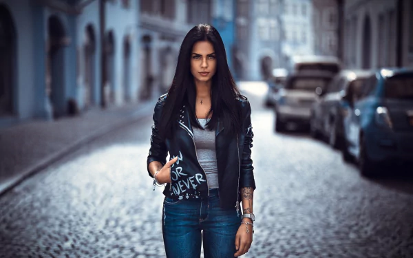 HD desktop wallpaper featuring model Marlen Valderrama Alvaréz with black hair, wearing a leather jacket, standing on a cobblestone street with a blurred background.