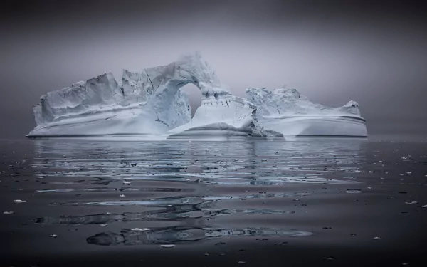4K Ultra HD wallpaper of a majestic iceberg with a natural arch, surrounded by calm water and enveloped in a soft, misty atmosphere.