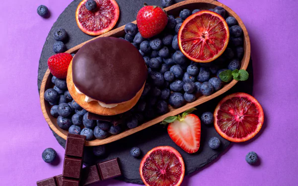 HD desktop wallpaper featuring a still life of chocolate-covered dessert, fresh blueberries, strawberries, and blood orange slices on a purple background.
