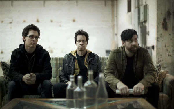 HD desktop wallpaper featuring three members of the band Chevelle, seated informally in a room with a rustic ambiance.