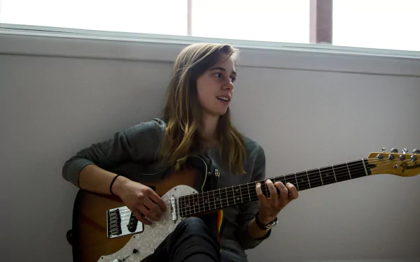 HD wallpaper of a person with a guitar, looking away thoughtfully, suitable as a serene desktop background.