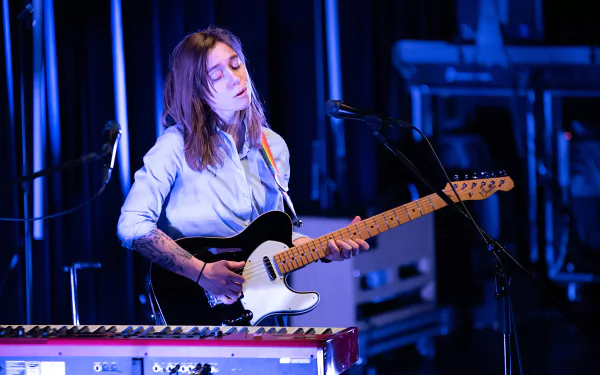 HD desktop wallpaper featuring an individual playing guitar on stage, with a serene expression, tagged as Julien Baker.