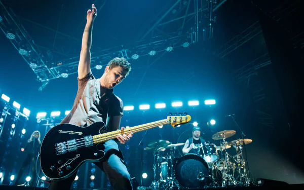 HD desktop wallpaper of Royal Blood musicians performing live on stage, featuring a dynamic shot of the bassist in the foreground and the drummer in the background, surrounded by vibrant stage lighting.