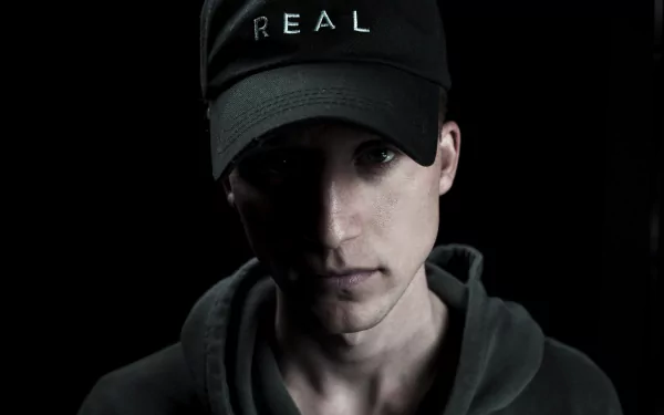 Man in black REAL cap and hoodie against dark background HD wallpaper.
