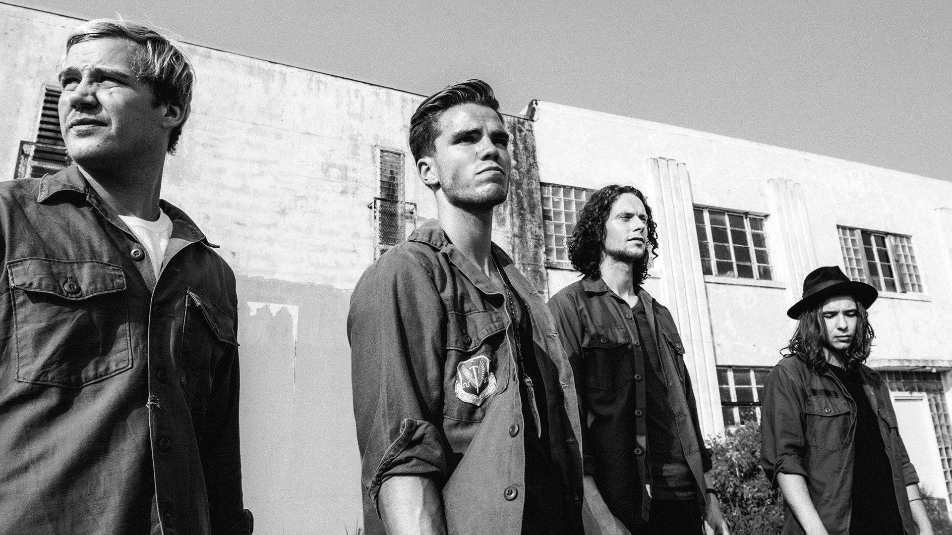 Black and white HD desktop wallpaper featuring the band KALEO, including a focused shot of a member, against an industrial building backdrop.