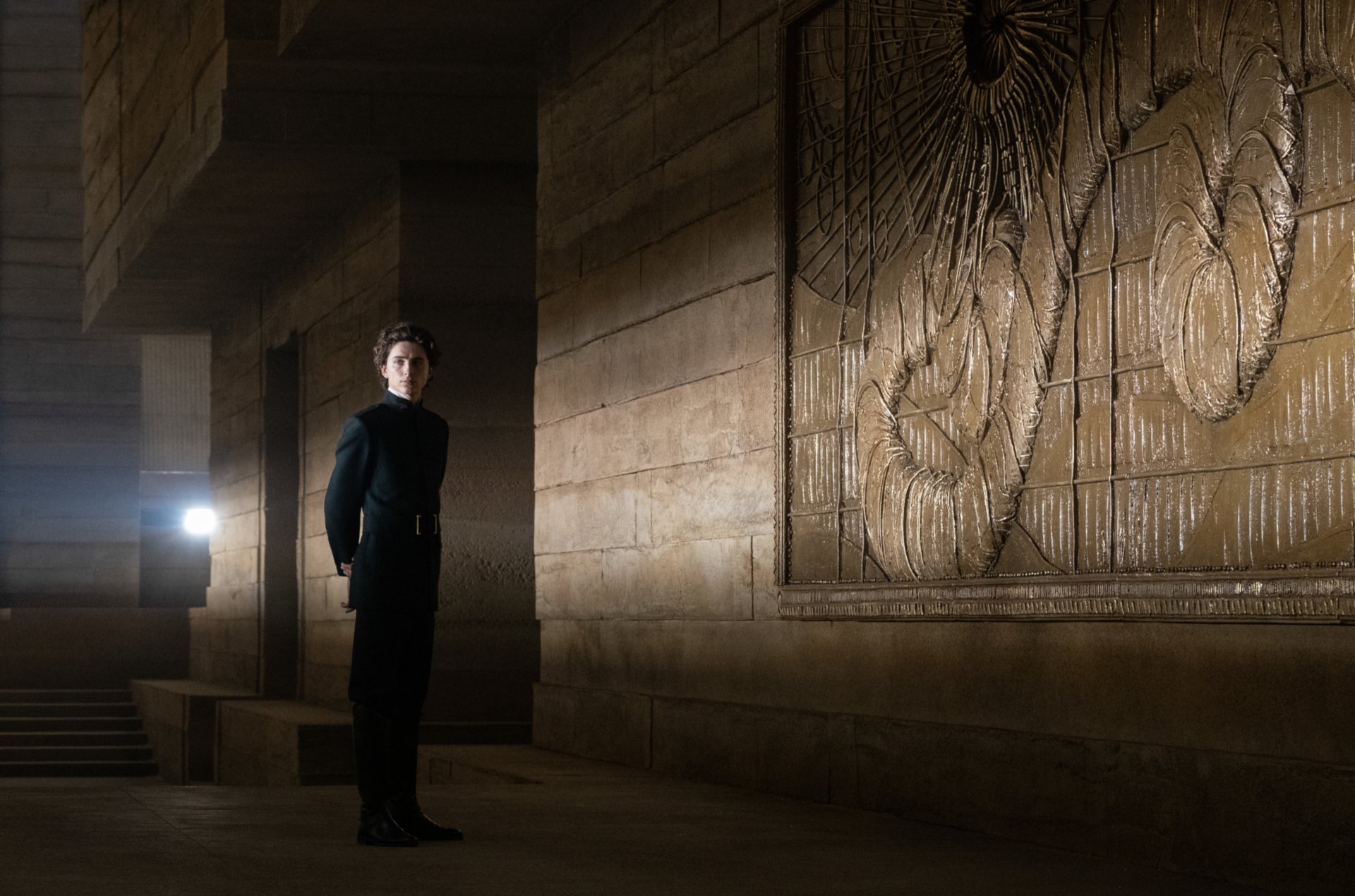 HD PC desktop wallpaper of Timothée Chalamet from the movie Dune (2021), standing in a dimly lit, ancient stone corridor with intricate wall carvings.