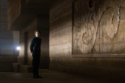 HD PC desktop wallpaper of Timothée Chalamet from the movie Dune (2021), standing in a dimly lit, ancient stone corridor with intricate wall carvings.