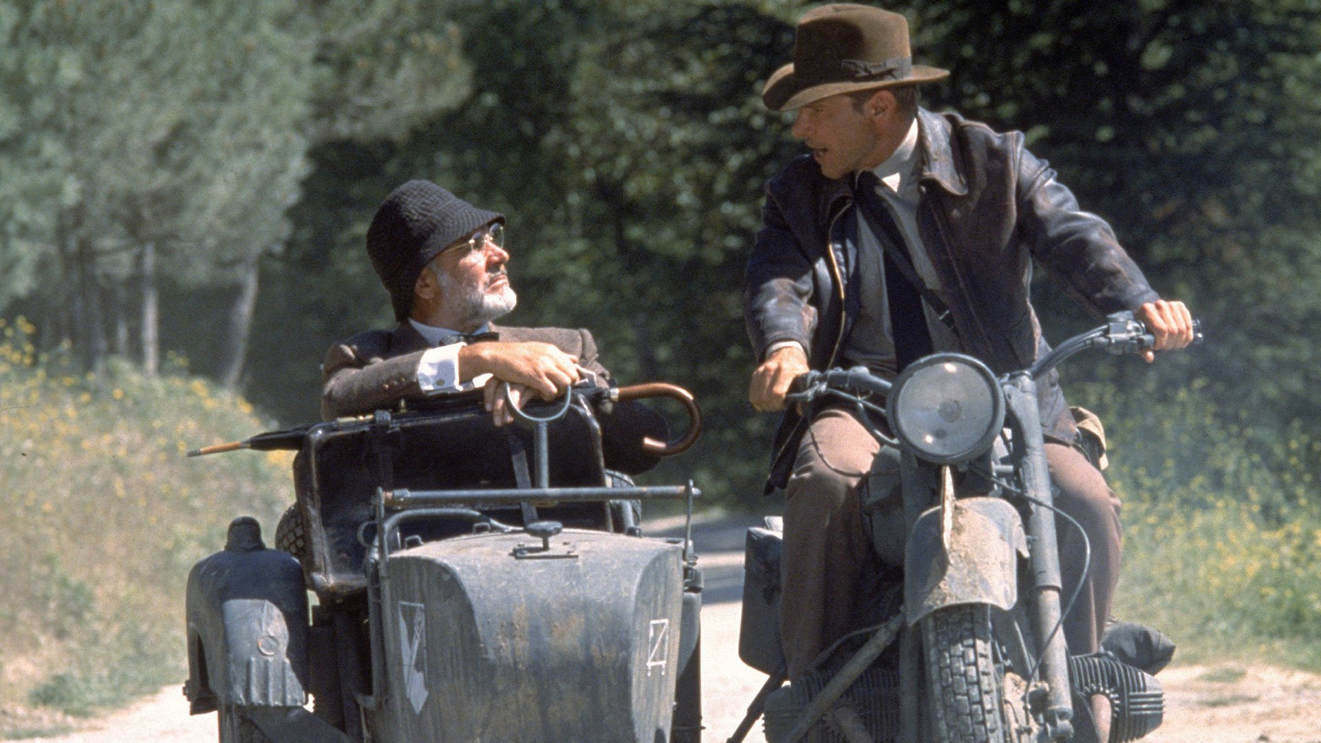 HD desktop wallpaper featuring Henry Jones Sr. (Sean Connery) and Indiana Jones (Harrison Ford) from the movie Indiana Jones and the Last Crusade riding a motorcycle with a sidecar.