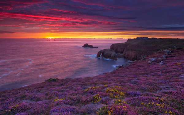 4K Ultra HD PC desktop wallpaper: nature coastline at sunset with violet heather-covered cliffs, a rocky sea arch, and a glowing orange-pink sky over the calm ocean.