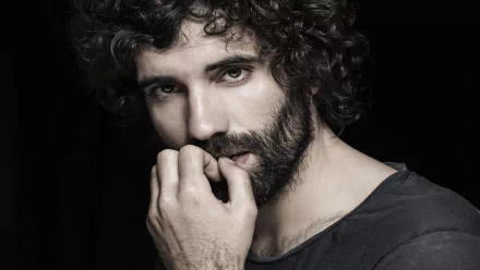 HD desktop wallpaper featuring celebrity Tamar Novas, showcasing his expressive gaze and curly hair against a dark background.