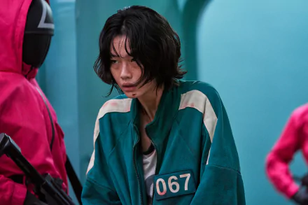 HD PC desktop wallpaper featuring Kang Sae-byeok from the TV show Squid Game, dressed in a green tracksuit with the number 067, surrounded by guards in red suits.