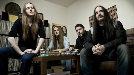 A HD desktop wallpaper featuring the band Carcass, showcasing four members casually seated in a room filled with vinyl records and eclectic decor.