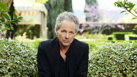 A serene HD desktop wallpaper featuring Lindsey Buckingham, captured in a lush garden setting, exuding a contemplative mood amidst vibrant greenery.