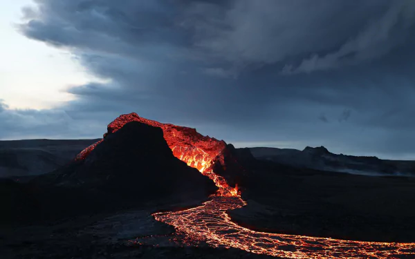 HD desktop wallpaper showing glowing lava flowing from an active volcano under a dramatic dark sky, capturing the raw power of nature.