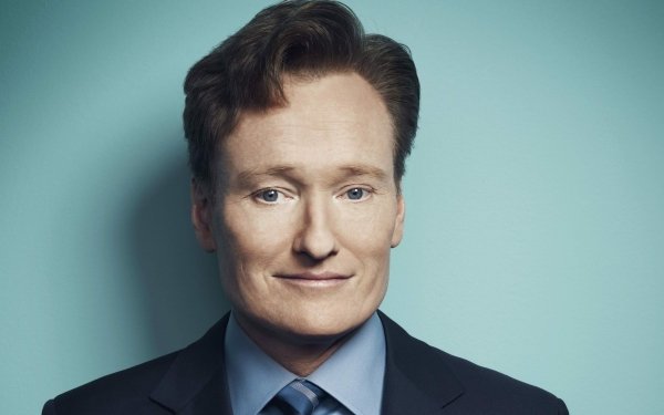 HD desktop wallpaper featuring a smiling man with red hair in a suit against a teal background.